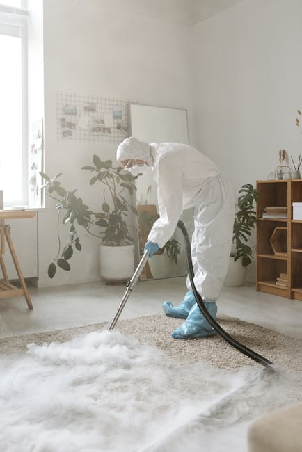 A woman using a yellow vacuum cleaner to deep clean a patterned area rug with floral motifs in a living room. The rug covers a wooden floor, and part of a red leather sofa is visible on the right. The